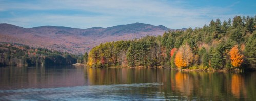 A serene lake surrounded by colorful autumn trees and mountains under a clear blue sky.