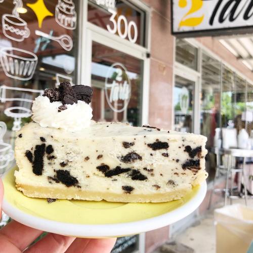 A slice of cookies and cream cheesecake topped with whipped cream and cookie pieces, held on a yellow plate.
