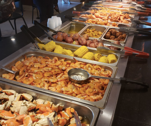 A buffet table featuring various seafood dishes, including shrimp, crab, corn, potatoes, and fried items.