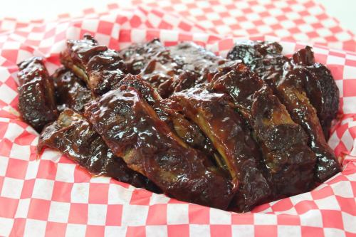 A close-up of glazed barbecue ribs served in a red and white checkered basket.