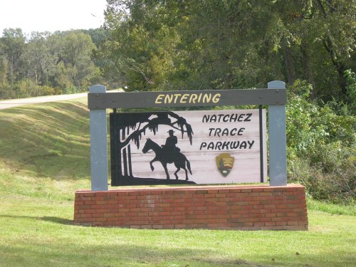 Sign marking the entrance to Natchez Trace Parkway, featuring a silhouette of a horse rider and trees.