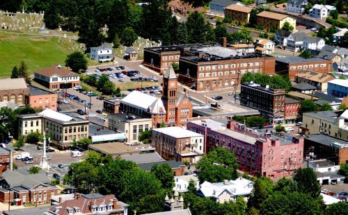 Aerial view of a small town featuring historic buildings, a clock tower, and surrounding greenery.