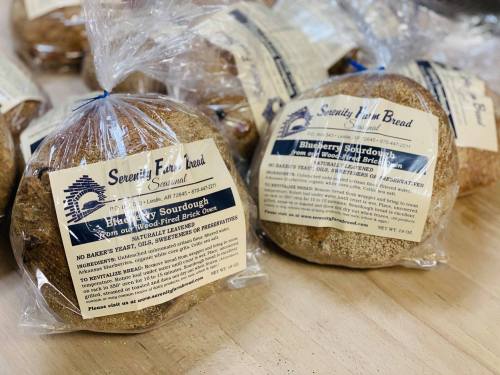 Two loaves of blueberry sourdough bread in clear packaging, labeled with "Serenity Farm Bread" and ingredient details.