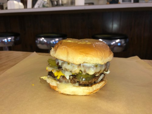 A juicy cheeseburger with melted cheese, pickles, and lettuce on a soft bun, placed on brown paper.