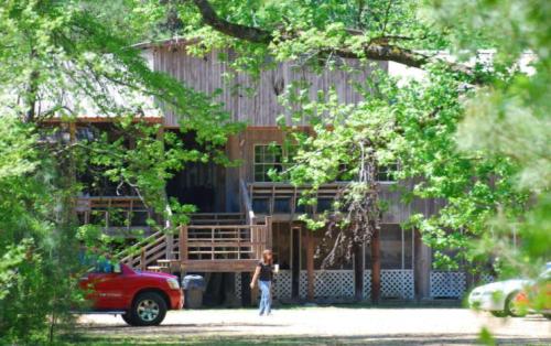 A wooden house surrounded by trees, with a person walking near a red truck in the foreground.