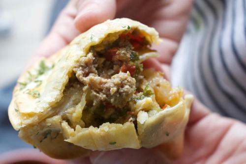 A close-up of a hand holding a stuffed pastry filled with meat, vegetables, and herbs, partially broken open.