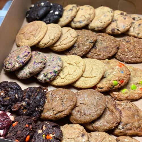 A box filled with a variety of cookies, including chocolate chip, oatmeal, and colorful sprinkle cookies.