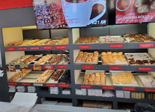 A display case filled with various donuts, including glazed, chocolate, and specialty options, alongside a menu board.
