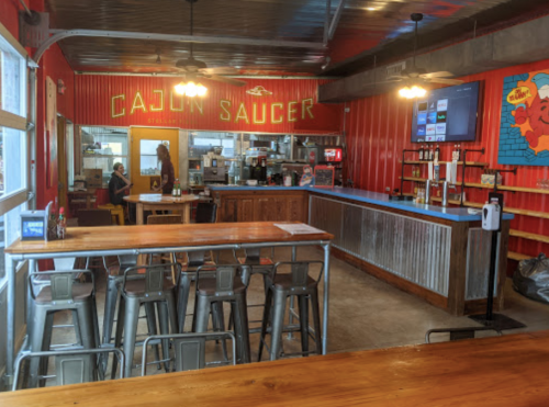 Interior of Cajun Saucer restaurant featuring colorful decor, a bar area with metal stools, and a cozy dining space.