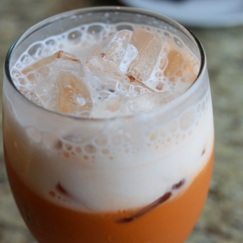 A close-up of a glass filled with iced tea, layered with milk and ice cubes, creating a creamy, refreshing drink.
