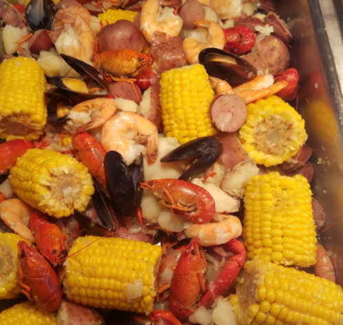 A colorful seafood boil featuring shrimp, crawfish, mussels, corn, potatoes, and sausage in a large tray.