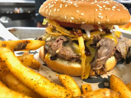 A close-up of a loaded burger with beef, cheese, and toppings, served with crispy fries on the side.