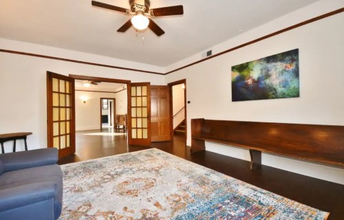 A spacious living room with a ceiling fan, wooden accents, and a colorful abstract painting on the wall.