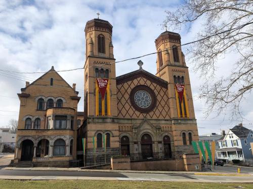 Historic church with twin towers and decorative banners, adjacent to a vintage building, set against a cloudy sky.