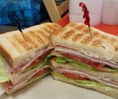 A stacked sandwich with layers of lettuce, tomato, and ham, held together with toothpicks, on a plate.