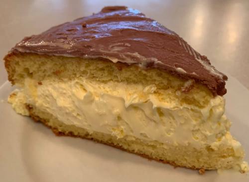 A slice of cake with a fluffy cream filling and a smooth chocolate frosting on top, served on a white plate.