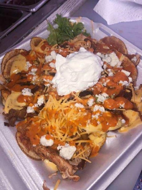A plate of nachos topped with cheese, sour cream, meat, and drizzled with sauce, garnished with lettuce.