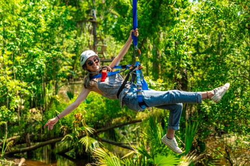 A woman in a helmet and harness enjoys zip-lining through a lush green forest.