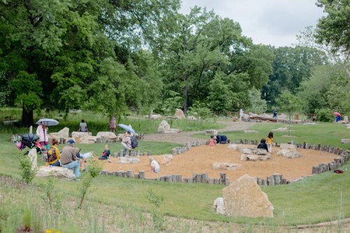 A playground with sandy areas and rocks, where families and children are enjoying the outdoors under cloudy skies.