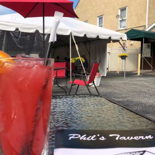 A refreshing drink sits on a table in front of Phil's Tavern, with a tent and chairs in the background.