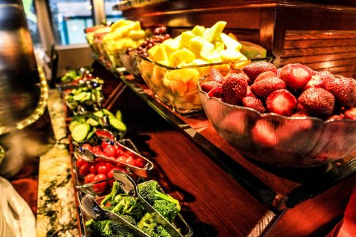 A colorful display of fresh fruits and vegetables in glass bowls, including strawberries, cucumbers, and assorted melons.
