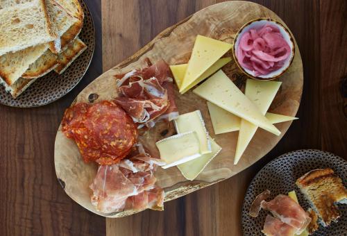 A wooden platter with assorted cheeses, cured meats, pickled onions, and toasted bread slices.