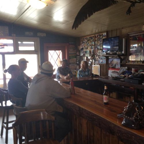 A cozy bar scene with patrons sitting at the counter, surrounded by wooden decor and photos on the walls.