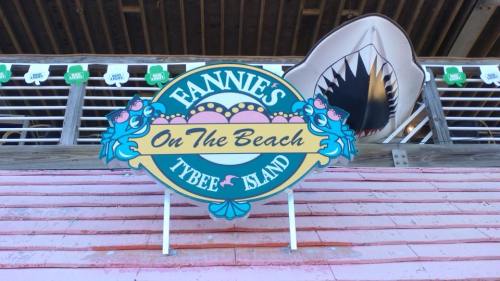 Sign for "Fannie's On The Beach" located on Tybee Island, featuring colorful design and a shark decoration above.
