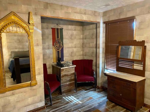 Cozy room featuring two red chairs, a wooden dresser, a mirror, and a chess set against a textured wall.