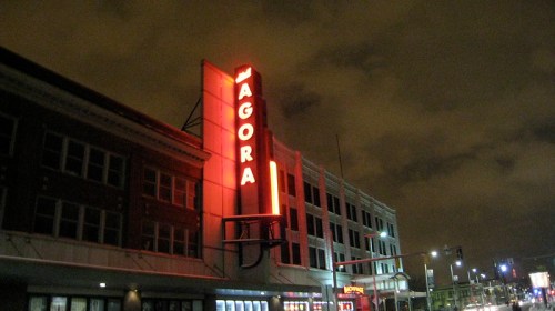 A building with a bright red "AGORA" sign illuminated against a cloudy night sky.