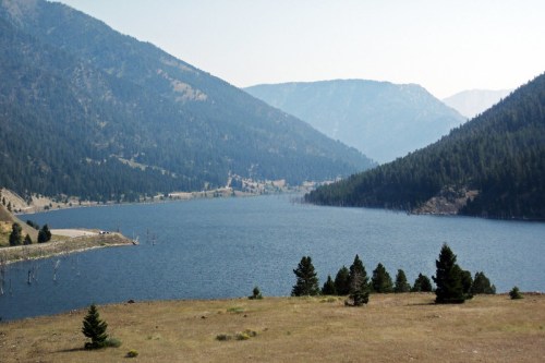 A serene lake surrounded by mountains and pine trees, with a clear blue sky above.
