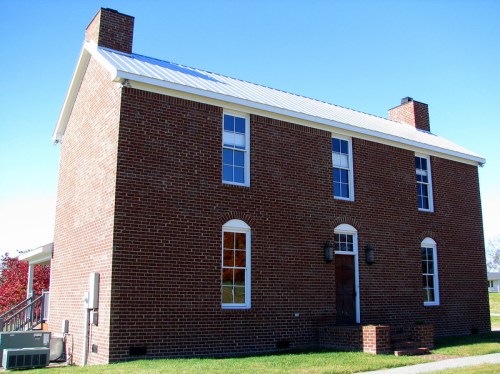 A two-story brick house with a metal roof, featuring multiple windows and a wooden front door.