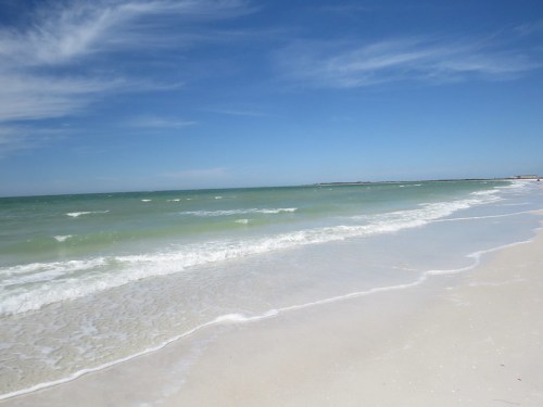 A serene beach scene with gentle waves lapping at the shore under a clear blue sky.