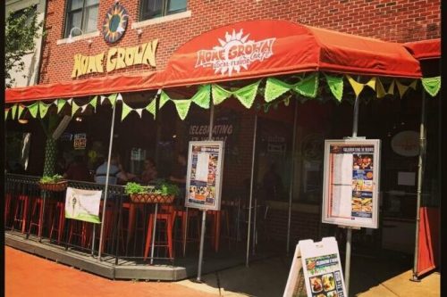 Exterior of Home Grown restaurant with a red awning, outdoor seating, and colorful signage on a sunny day.