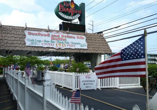 Sign for The Bonfire Restaurant featuring a seafood and prime rib buffet, with American flags and a waiting area.