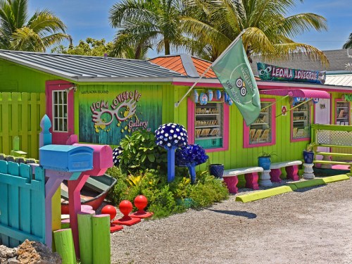 Colorful art gallery with vibrant green and pink walls, surrounded by palm trees and whimsical decorations.