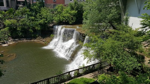 A serene waterfall cascading over rocks into a calm pond, surrounded by lush greenery and trees.