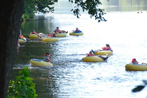 A group of people in yellow inner tubes floating on a calm river, surrounded by trees and sunlight.