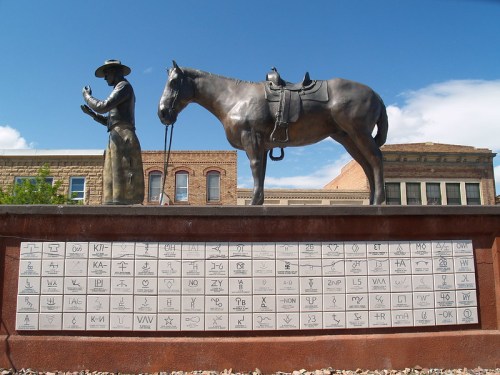 A bronze statue of a cowboy with a horse, accompanied by a plaque featuring various symbols and characters.