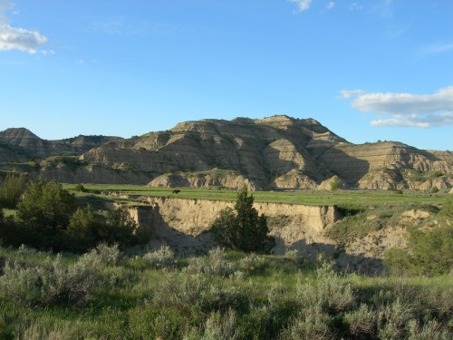 A scenic view of layered hills and grassy plains under a blue sky with scattered clouds.
