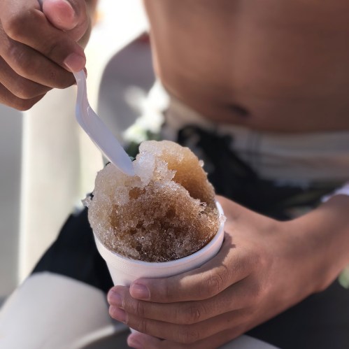 A person holds a cup of shaved ice with a spoon, enjoying a sweet treat on a sunny day.