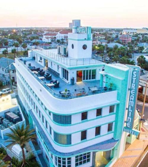Aerial view of the Streamline Hotel, featuring a modern design and rooftop terrace, surrounded by palm trees and cityscape.