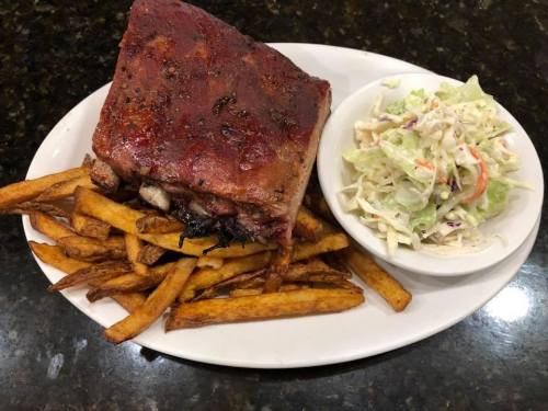 A plate featuring a large piece of grilled meat, crispy fries, and a side of coleslaw.