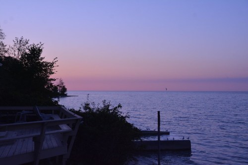 A serene lakeside view at dusk, with soft purple hues in the sky and calm water reflecting the colors.