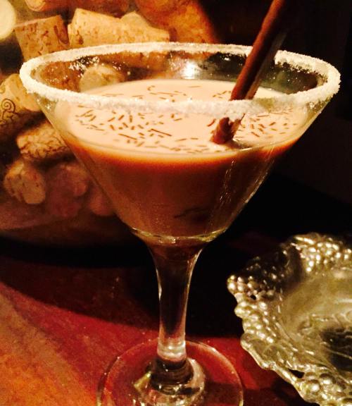 A chocolate cocktail in a sugar-rimmed martini glass, garnished with chocolate sprinkles and a stirrer.