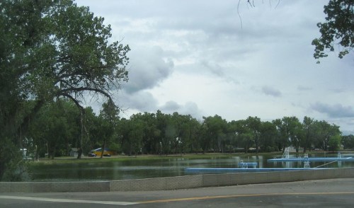 A serene park scene featuring a calm lake surrounded by trees under a cloudy sky.