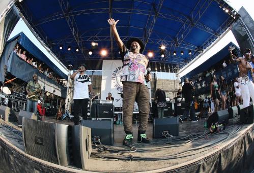 A lively music performance on stage with artists engaging the crowd, surrounded by fans and vibrant stage setup.