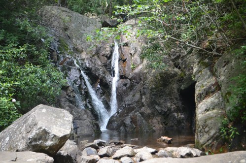 A serene waterfall cascading over rocks into a calm pool, surrounded by lush greenery and boulders.