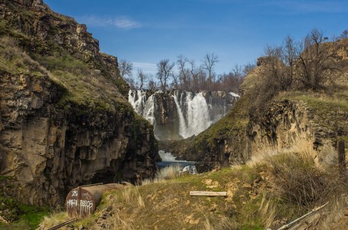 A scenic view of a waterfall cascading between rocky cliffs under a clear blue sky.
