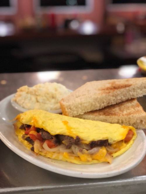 A plate featuring a cheese omelet with vegetables, served with toast and a side of grits.